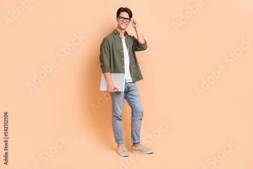 Full length photo cadre of young optimistic man student working remote wear spectacles hold netbook programmer isolated on beige color background