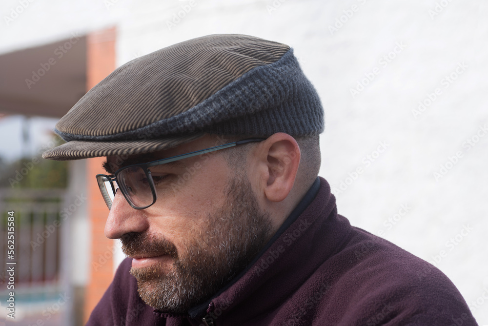 man in brown and gray corduroy and wool beret. man in his forties, beard and glasses, wearing a maroon fleece, portrait looking at the camera, open air, in the background a house.