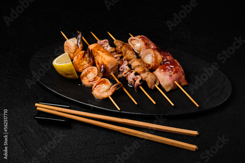 Japanese Seafood Skewers. Black tiger shrimp, scallop and salmon fillet, octopus served with sauce. Yakitori isolated on black concrete background photo