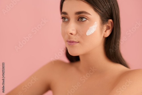 Feminine young lady with cream on face looking away in pink studio