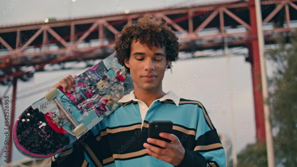 Contemporary skateboarder texting phone closeup. Curly man carrying longboard