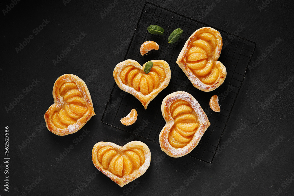 Puff pastry cake in the shape of a heart with tangerine slices and mint leaves on a dark table. top view, copy space
