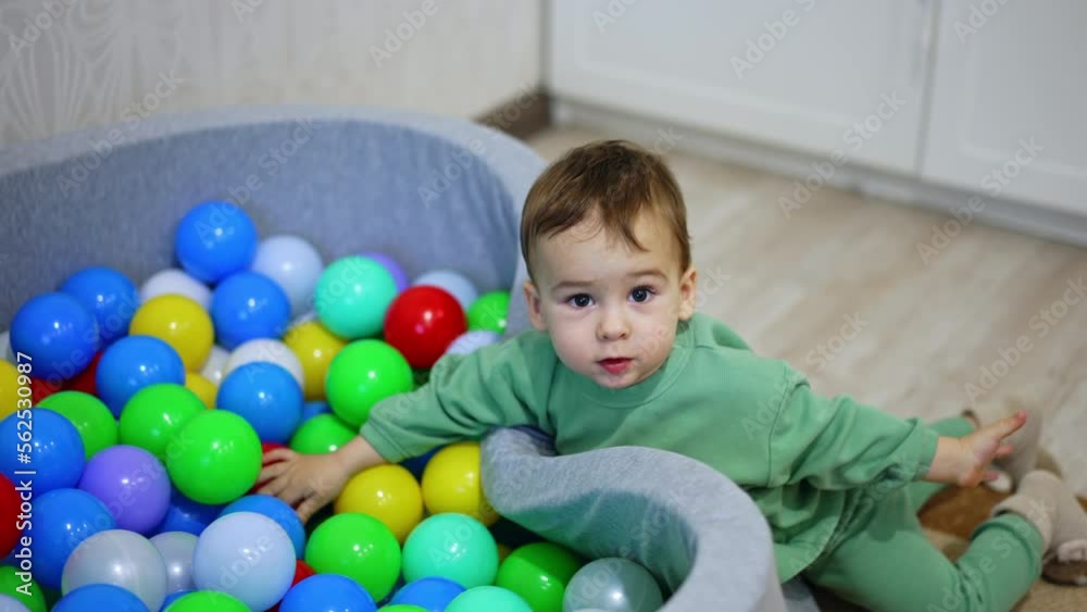 Lovely kid plays at the dry pool filled with colorful toys. Small child plays indoors. Top view. Lovely kid plays at the dry pool filled with colorful toys. Small child plays indoors. Top view.