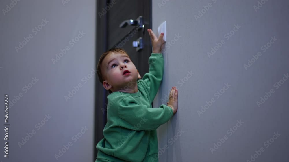 Curious baby boy reaches the light switch. Sweetest kid turns the light on and off in the room.