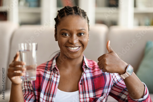 Poditive young black woman drinking water at home, copy space