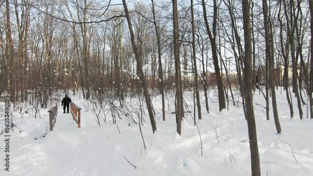 Front facing Man snowshoeing in the woods, on a trail covered of snow and crossing a small bridge in winter Front facing Man snowshoeing in the woods, on a trail covered of snow and crossing a small bridge in winter