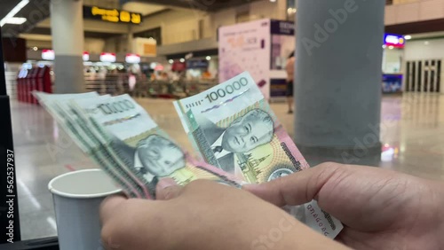 Bangkok, Thailand - Circa January, 2023 : Female hand counting 100000 lao kip money at the airport with blurred check in counters in background. Travel and tourism concept photo