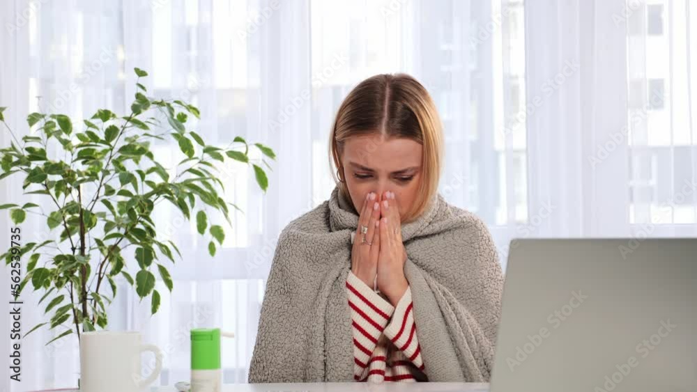 Sick woman wrapped in blanket sniffs coughs while works at the laptop. Allergic woman blowing nose in tissue girl got flu caught cold sneeze in tissue having allergy symptoms coughing holding napkin. Sick woman wrapped in blanket sniffs coughs while works at the laptop. Allergic woman blowing nose in tissue girl got flu caught cold sneeze in tissue having allergy symptoms coughing holding napkin.