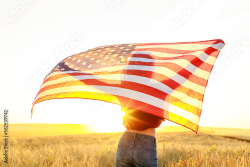 woman in field holding USA stars and stripes flag in golden sunset evening sunshine