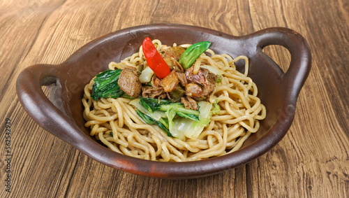 Plate of noodles with chicken and vegetables on wooden table.