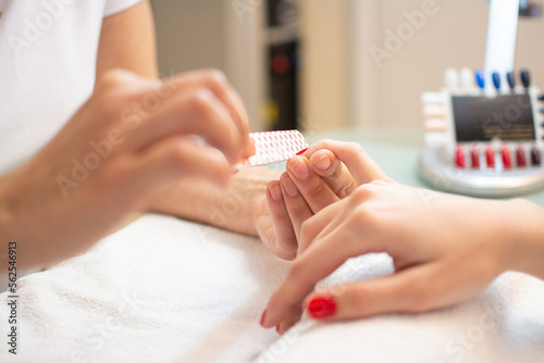 Closeup of a woman's hand in a nail salon receiving a manicure by a beautician with nail file. photo