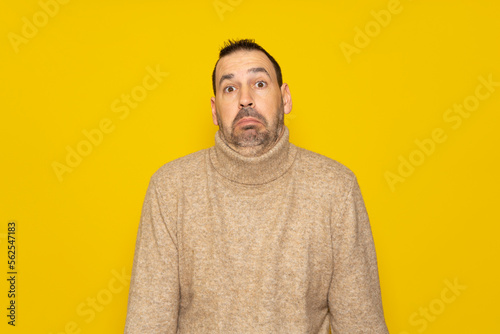 Bearded latino man doubting and shrugging, concept of indecision and insecurity, uncertain about something. Isolated on orange studio background.