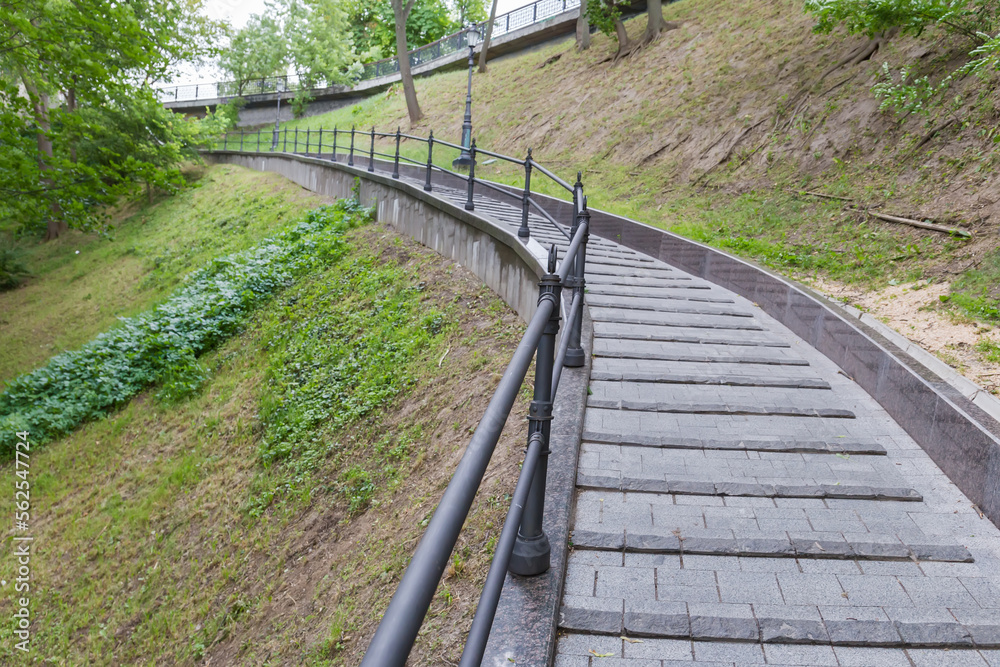Paved path with railings on hillside in summer city park