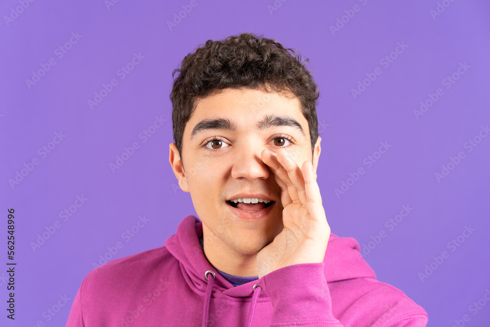 Hispanic boy whispering or telling a secret while looking at camera isolated on purple background