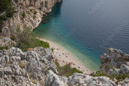 Scenic Nugal Beach-pebbly beach preferred by nudists-below a huge vertical rock wall towering above turquoise water at Gradac viewpoint with a stunning view to the coastline and Mount Biokovo, Croatia