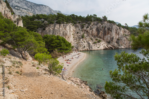 Fototapeta Naklejka Na Ścianę i Meble -  Scenic Nugal Beach-pebbly beach preferred by nudists-below a huge vertical rock wall towering above turquoise water at Gradac viewpoint with a stunning view to the coastline and Mount Biokovo, Croatia