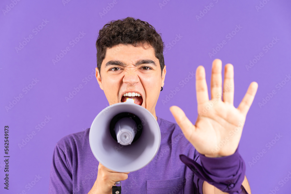Angry protestor man shouting on megaphone and making stop gesture with hand isolated on purple background. Feminism and equality concept Angry protestor man shouting on megaphone and making stop gesture with hand isolated on purple background. Feminism and equality concept