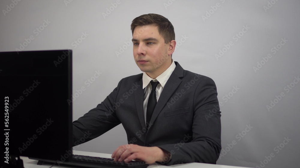 A young businessman is sitting in the office and typing on a computer keyboard. A man in a suit sits at a computer. A young businessman is sitting in the office and typing on a computer keyboard. A man in a suit sits at a computer.