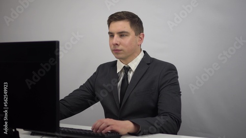 A young businessman is sitting in the office and typing on a computer keyboard. A man in a suit sits at a computer. © Vital9c