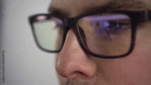 Young man surfs the internet. Reflection of a pc monitor in glasses. The IT specialist looks at the monitor attentively. Glasses close-up.