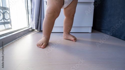 Toddler doing first steps on wooden floor at home, baby's feet walking