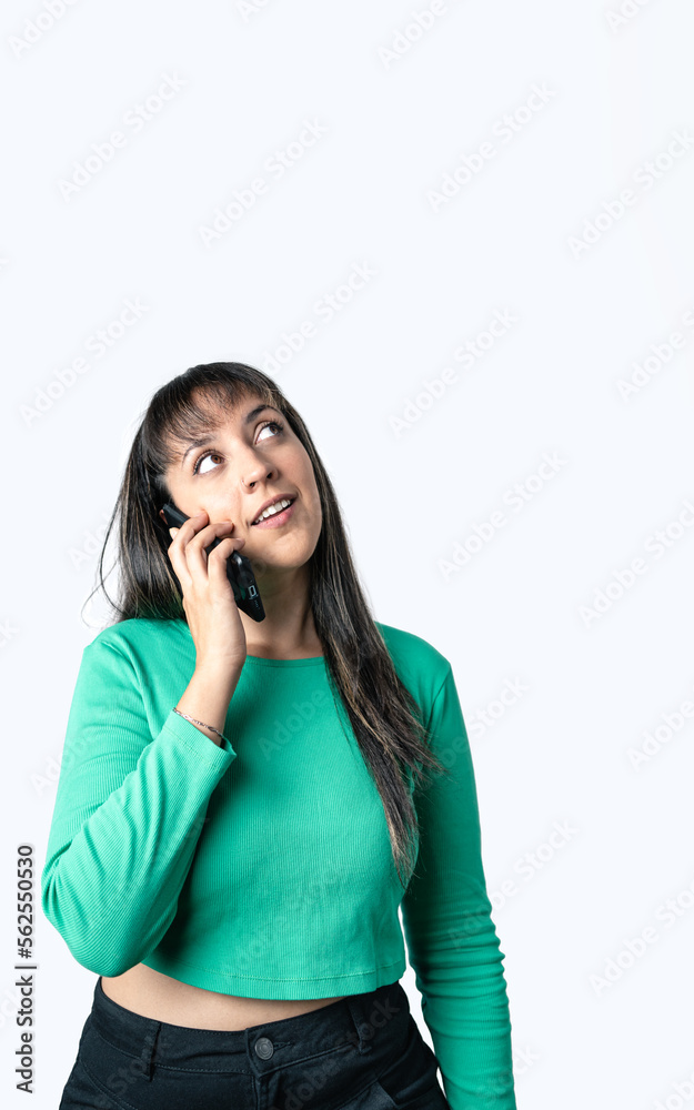 Latin woman dressed with casual clothes is talking on the phone and looking up on a white background. Vertical shot with copy space Latin woman dressed with casual clothes is talking on the phone and looking up on a white background. Vertical shot with copy space