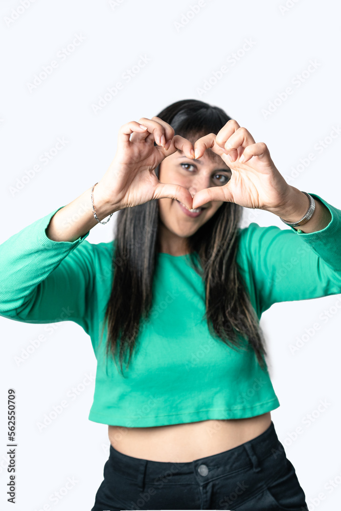 Hispanic woman making a heart shape with her hands over her face. Isolated white background.