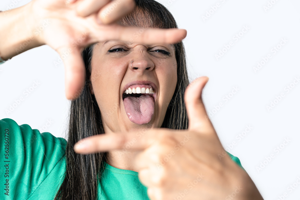 Young woman making a frame with her fingers and sticking out her tongue over isolated white abckground Young woman making a frame with her fingers and sticking out her tongue over isolated white abckground
