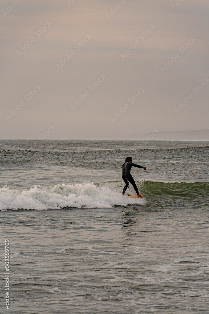 surfer on the beach under a beautiful sunset in front of the pier with big sea waves surfer on the beach under a beautiful sunset in front of the pier with big sea waves