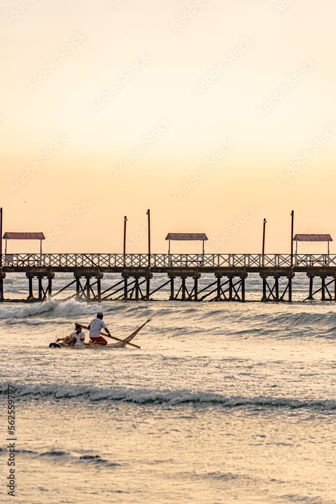 fisherman on the beach under a sunset next to a pier