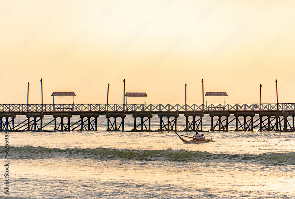 fisherman on the beach under a sunset next to a pier