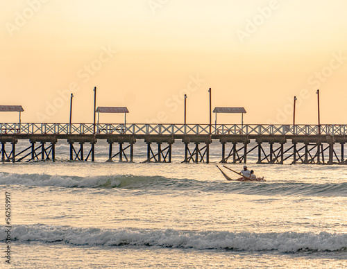 fisherman on the beach under a sunset next to a pier