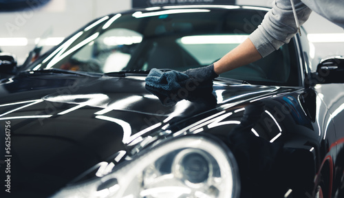 Man using a microfiber cloth to apply ceramic coating onto a shiny expensive black car. Unrecognizable person in protective gloves. High quality photo © PoppyPix