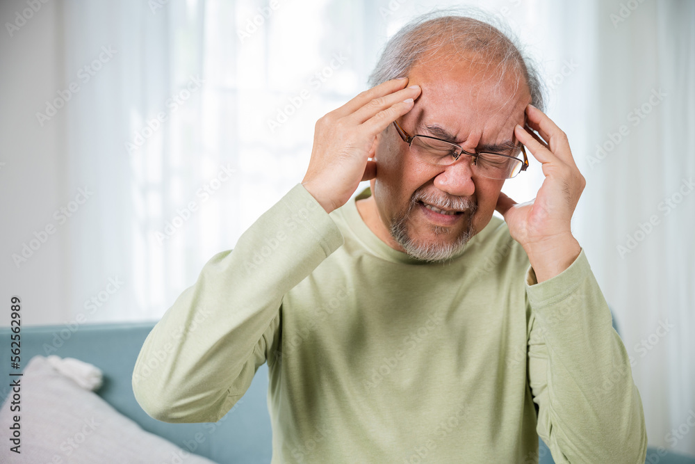 Headache. Sad Asian senior man chronic migraine pain massaging, old man holds head with hand for headache disease in living room at home, Old age health problems, healthcare Headache. Sad Asian senior man chronic migraine pain massaging, old man holds head with hand for headache disease in living room at home, Old age health problems, healthcare