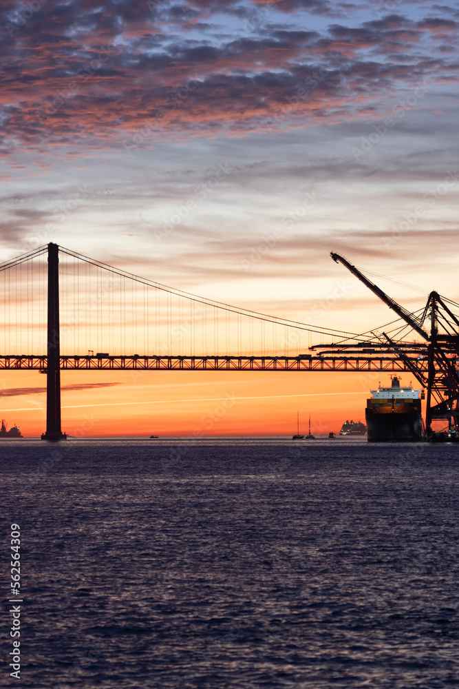 Lisbon 25th of April Bridge at sunset and industrial working cranes