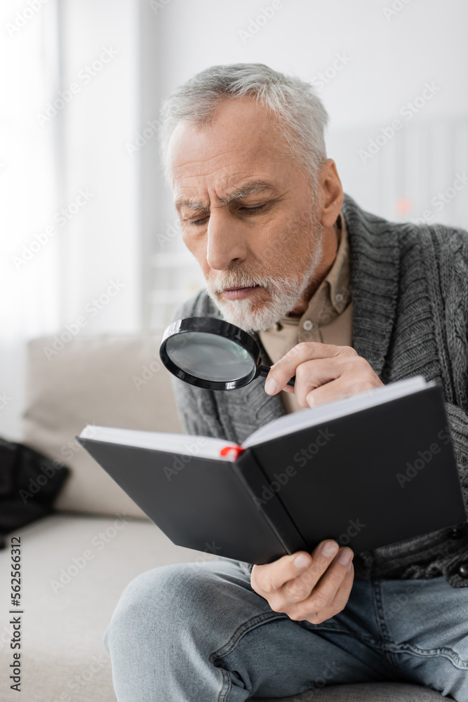 aged man with alzheimer syndrome looking in notebook through magnifier while sitting at home. aged man with alzheimer syndrome looking in notebook through magnifier while sitting at home.
