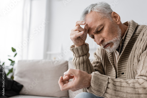 grey haired man with parkinson syndrome and tremor in hands sitting with closed eyes on couch at home.