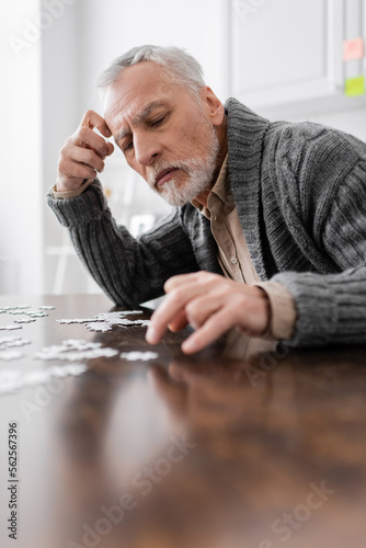 aged man with parkinson disease and trembling hands combining jigsaw puzzle on blurred foreground.