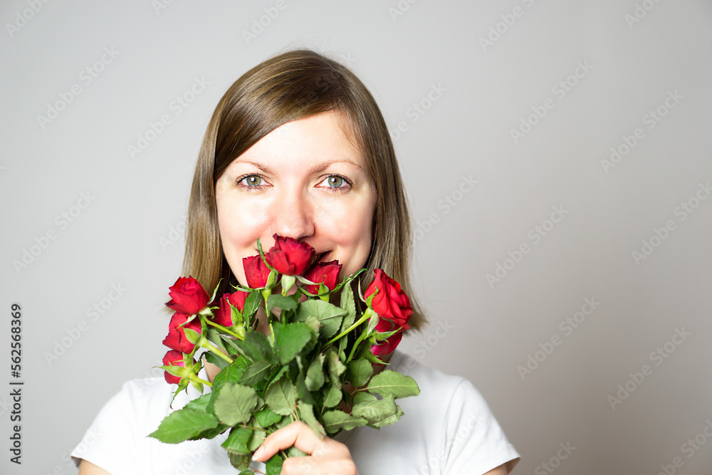A portrait of an attractive smiling girl with a bouquet of red roses in the hands. 