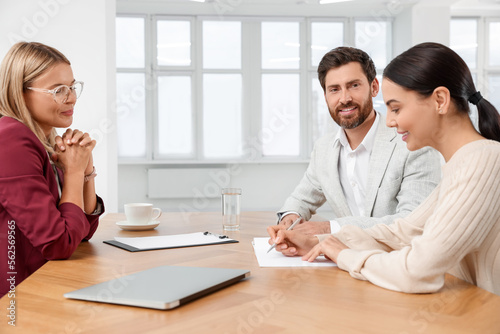 Real estate agent and couple signing contract at table in new apartment