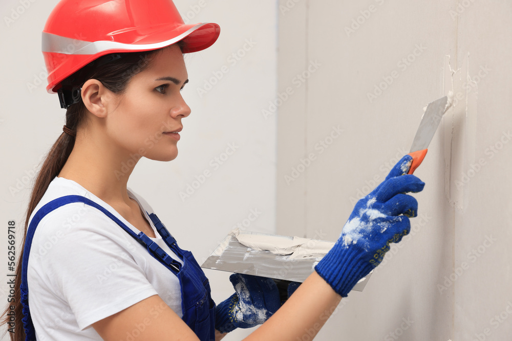 Professional worker in hard hat plastering wall with putty knives indoors Professional worker in hard hat plastering wall with putty knives indoors