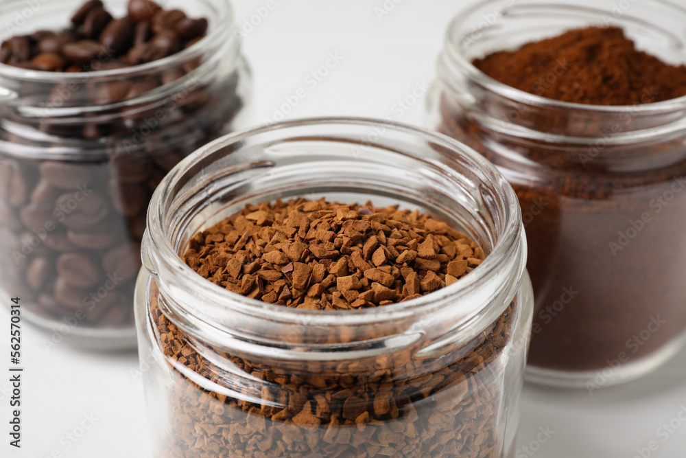 Jars with instant, ground coffee and roasted beans on white table, closeup Jars with instant, ground coffee and roasted beans on white table, closeup