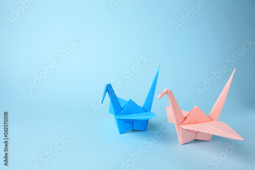 Origami art. Colorful handmade paper cranes on light blue background, space for text