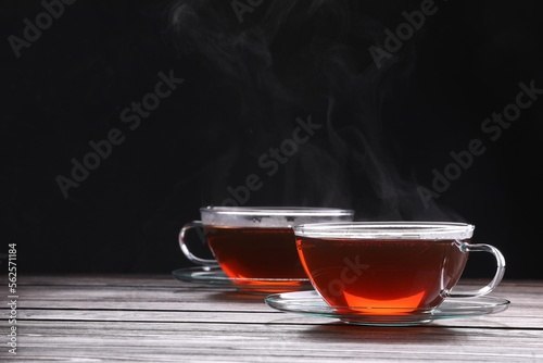 Glass cups with tea on wooden table against black background, space for text