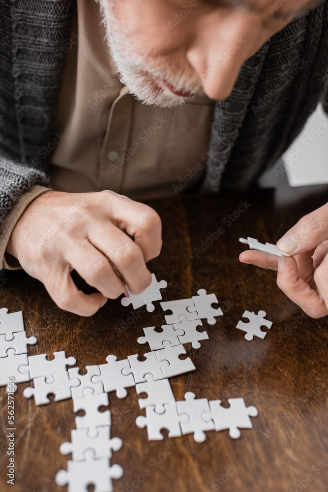 cropped view of senior man with parkinson disease and tremor in hands combining jigsaw puzzle on table at home. cropped view of senior man with parkinson disease and tremor in hands combining jigsaw puzzle on table at home.