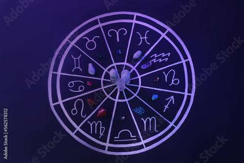 Natural stones for zodiac signs and drawn astrology chart on dark blue background, flat lay. Color tone effect