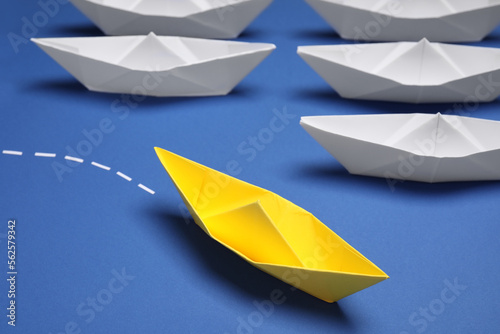 Yellow paper boat floating away from others on blue background  closeup. Uniqueness concept