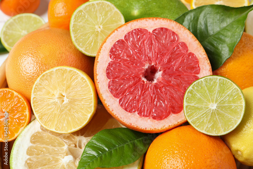 Different ripe citrus fruits with green leaves as background  closeup