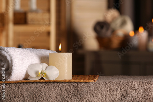 Spa composition with candle, orchid flower and rolled towel on massage table in wellness center, space for text
