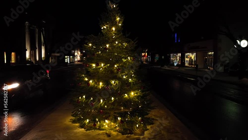 Slow aerial orbit around Christmas tree with lights on main street of Wellsboro Pennsylvania. Car headlights illuminate light snow flurries on cold, dark Christmas morning. photo